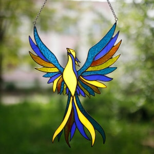 A stained glass suncatcher in the shape of a blue-yellow phoenix bird on the window.