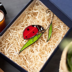 ladybug on two leaves of stained glass  in gift box with straw filler. near the box on the table a little candle