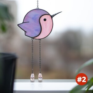 Suncatcher made with stained glass in the shape of a cartoon Hummingbird. purple hummingbird has a pink belly with long chain-legs