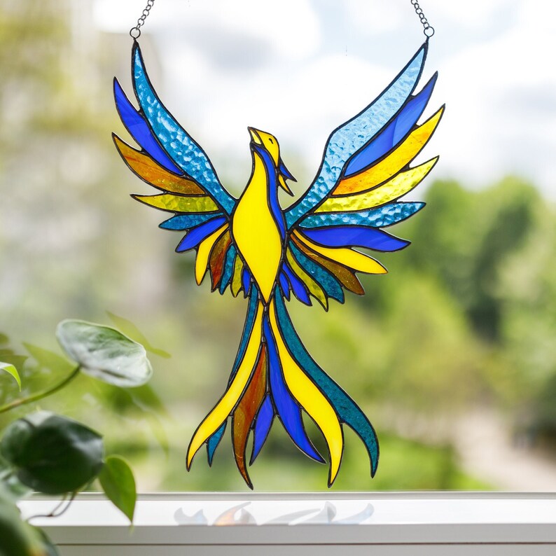 A stained glass suncatcher in the shape of a blue-yellow phoenix bird on the window.