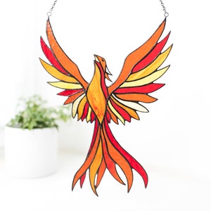 A stained glass suncatcher in the shape of a red-orange phoenix bird.