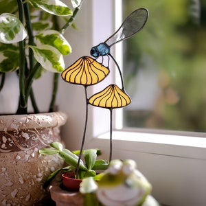 suncatcher in the form of two orange mushrooms with veins on which sits a dragonfly with blue wings in a plant vase