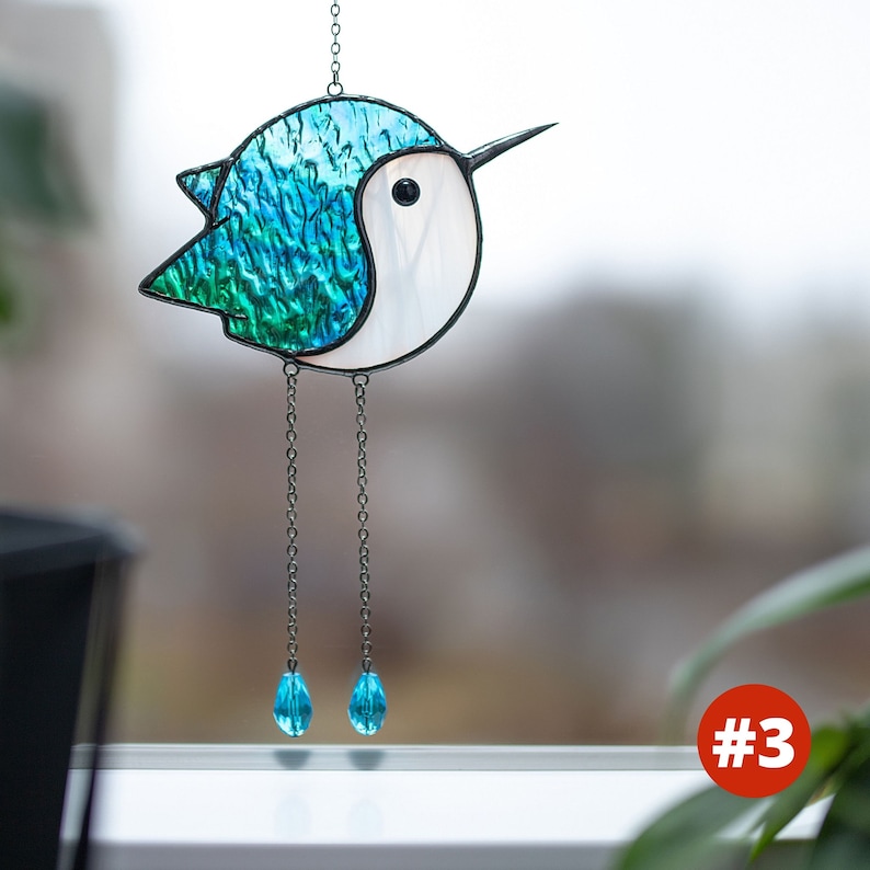 Suncatcher made with stained glass in the shape of a cartoon Hummingbird. emerald hummingbird has a white belly with long chain-legs