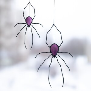 A stained glass suncatcher shaped like a spider on a web.