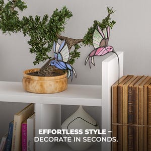 May include: Two stained glass hummingbird decorations, one blue and one pink, are displayed near a small bonsai tree in a pot. The text "EFFORTLESS STYLE - DECORATE IN SECONDS" is at the bottom of the image. The decorations are on a white shelf.