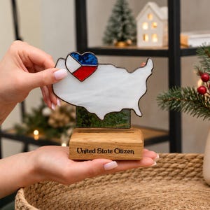 May include: A stained glass map of the United States in white with a heart-shaped accent featuring the Czech Republic flag colours. The map is mounted on a rectangular wooden base with the text United State Citizen engraved on the front.