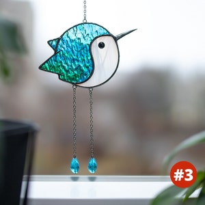 Suncatcher made with stained glass in the shape of a cartoon Hummingbird. emerald hummingbird has a white belly with long chain-legs