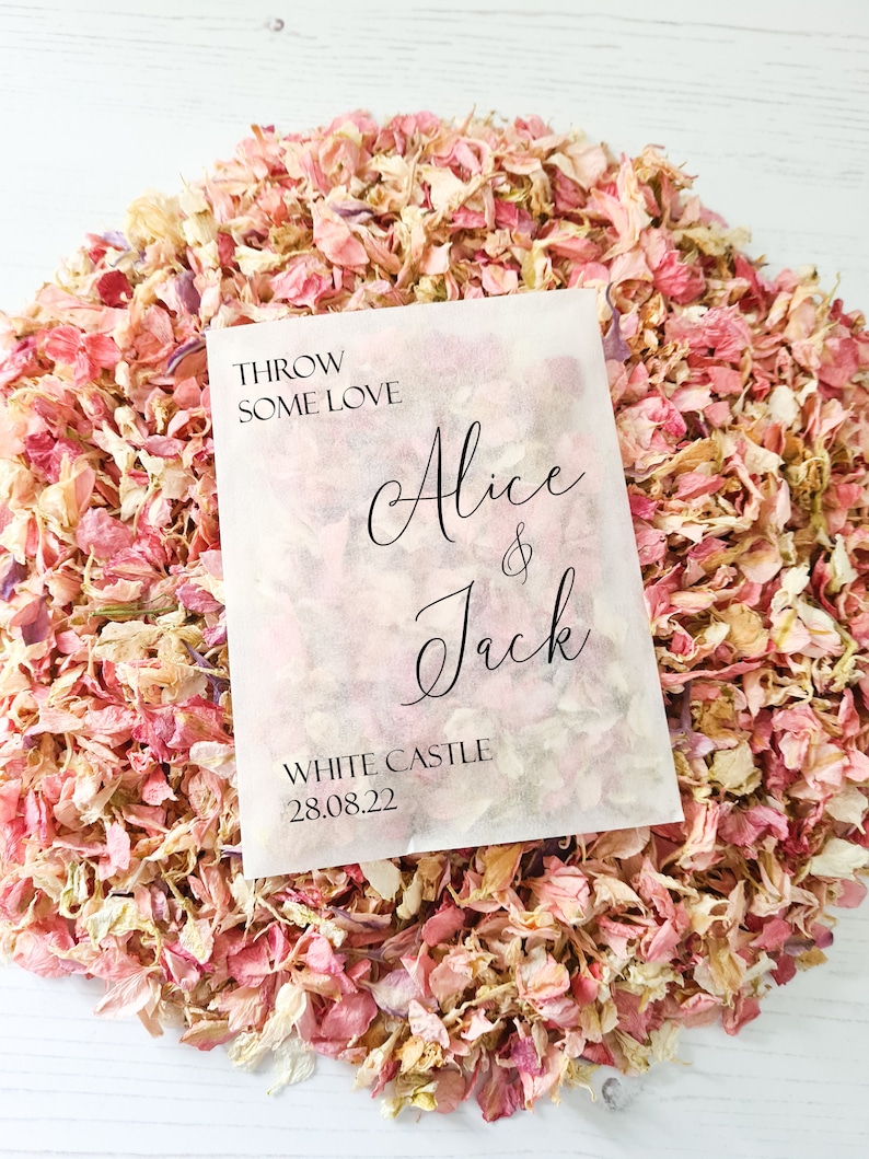 May include: A white paper bag filled with pink and white flower petals. The bag has black text that reads "Throw some love Alice & Jack White Castle 28.08.22".