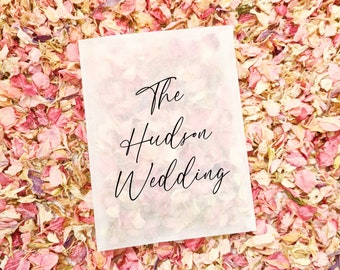 May include: A white paper bag with the text "The Hudson Wedding" written in black calligraphy on a background of pink and white flower petals.