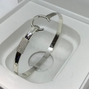 May include: A silver bangle bracelet with a textured band and a hook clasp.