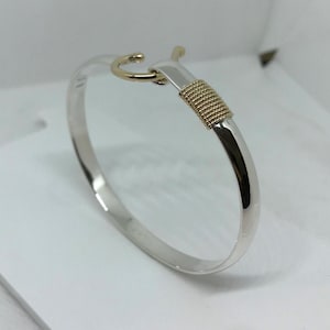 May include: A silver bangle bracelet with a gold hook clasp and a gold band with a textured design.