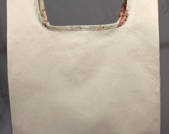 May include: A white canvas tote bag with a floral print lining. The bag has a wide opening and is hanging from a white rod.