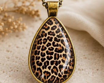 Puede incluir: Un collar con colgante en forma de lágrima que presenta un estampado de leopardo en tonos marrón y negro, engastado en un marco de metal color bronce antiguo y suspendido de una cadena de eslabones a juego.