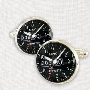 Puede incluir: Gemelos plateados con esfera negra de altímetro. La esfera muestra números blancos, agujas y el texto "ALTIMETER" y "MWC". El altímetro indica 0090. Un accesorio elegante.