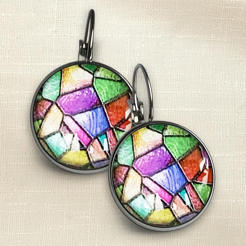 Puede incluir: Un par de pendientes redondos con cierre de palanca que presentan un patr&oacute;n de vidrieras de colores con segmentos en verde, morado, azul, amarillo y rojo. Los marcos circulares son de metal oscuro e imitan el aspecto del vidrio emplomado.