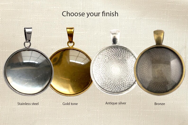 May include: Four circular pendant trays with bails, labeled Choose your finish. The options are stainless steel, gold tone, antique silver, and bronze. Each pendant features a smooth, rounded surface, with the antique silver and bronze showing a textured pattern.