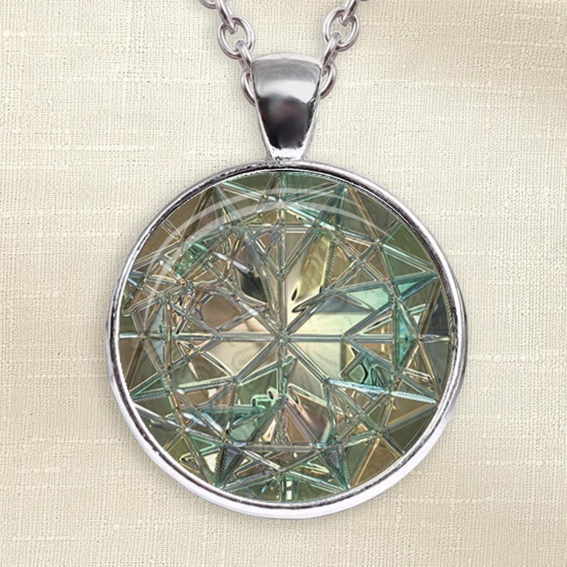 May include: A circular pendant necklace featuring a silver-toned metal frame and a faceted glass insert. The insert displays a complex geometric pattern with intersecting lines in shades of pale green, gold, and iridescent silver, suspended from a chain.