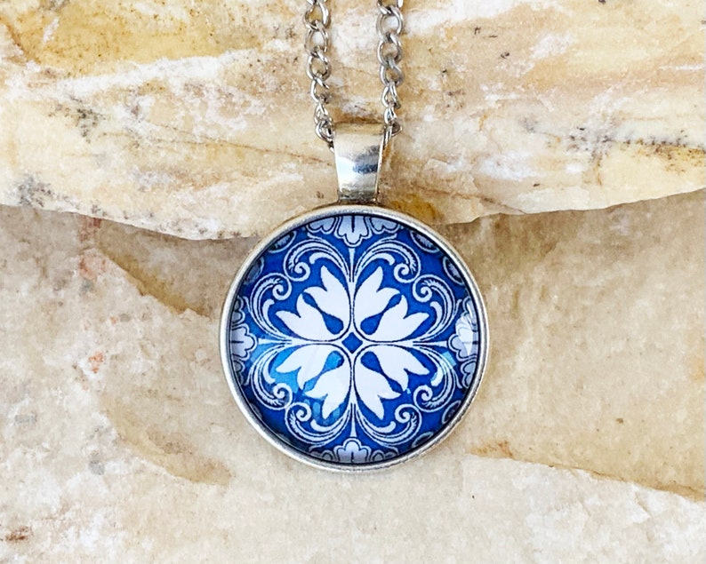 May include: A silver chain necklace with a blue and white patterned glass pendant. The pendant features a floral design with white flowers on a blue background.