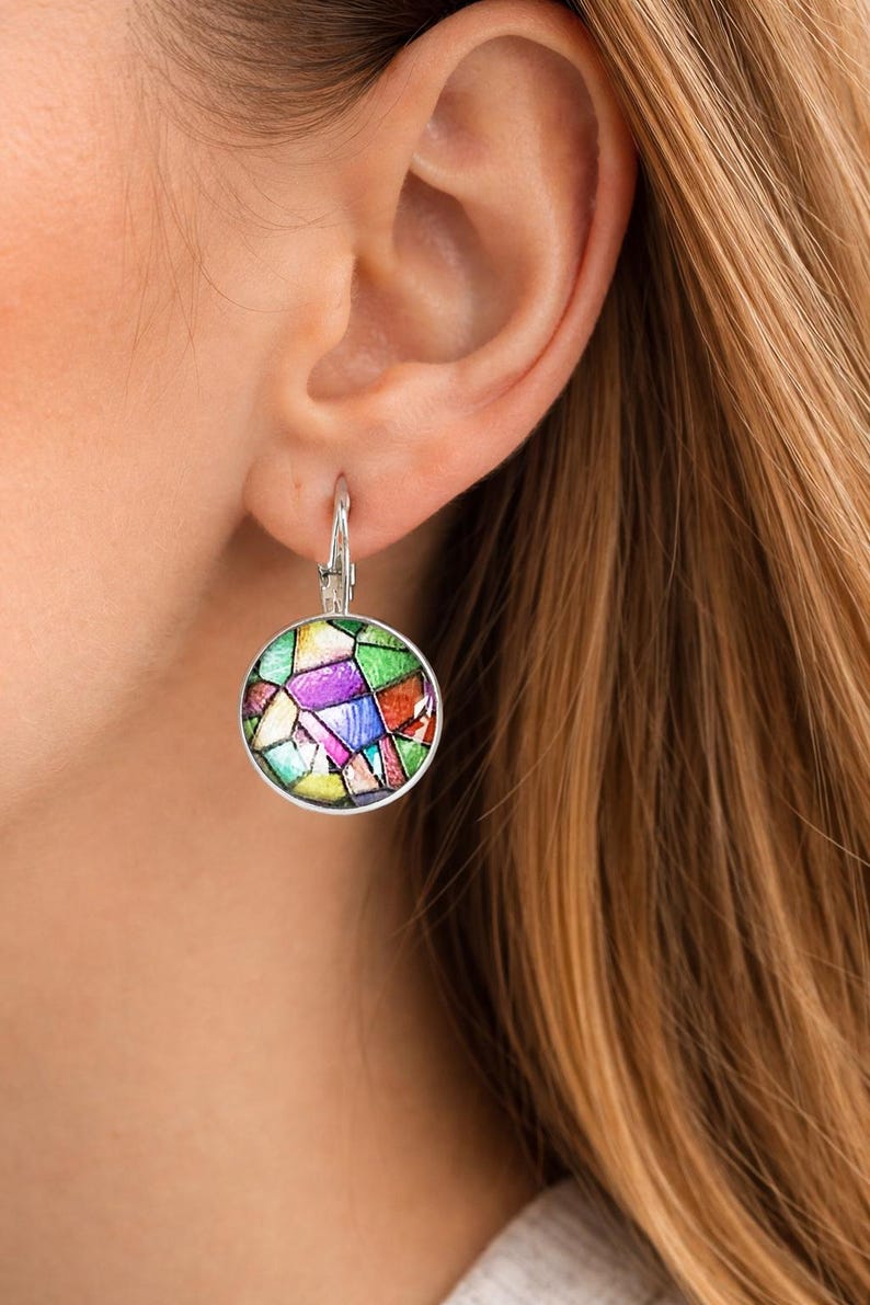 Puede incluir: Un pendiente redondo de plata con cierre de palanca que presenta un patr&oacute;n de mosaico multicolor con segmentos en verde, morado, naranja, azul y amarillo. El dise&ntilde;o circular est&aacute; enmarcado en plata pulida, creando un efecto de vidriera.