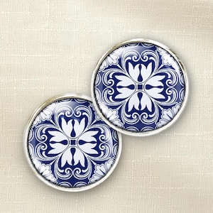 May include: Two circular buttons featuring a deep blue and white floral pattern. Each button has a polished silver-tone metal rim surrounding the intricate, symmetrical design of stylized petals and swirling scrollwork motifs.