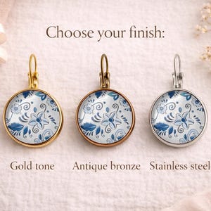 May include: Three round leverback earrings featuring a blue and white floral pattern. The earrings are displayed in three different finishes: gold tone, antique bronze, and stainless steel. The text "Choose your finish:" is centered above.