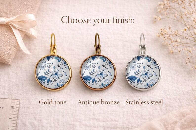 May include: Three round leverback earrings featuring a blue and white floral pattern. The earrings are displayed in three different finishes: gold tone, antique bronze, and stainless steel. The text "Choose your finish:" is centered above.