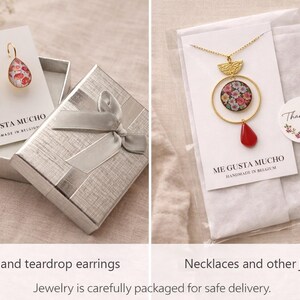 May include: A pair of teardrop leverback earrings with a floral pattern on white display cards labeled ME GUSTA MUCHO, alongside a gold-tone necklace featuring a circular floral pendant and a red teardrop charm in a clear plastic sleeve.