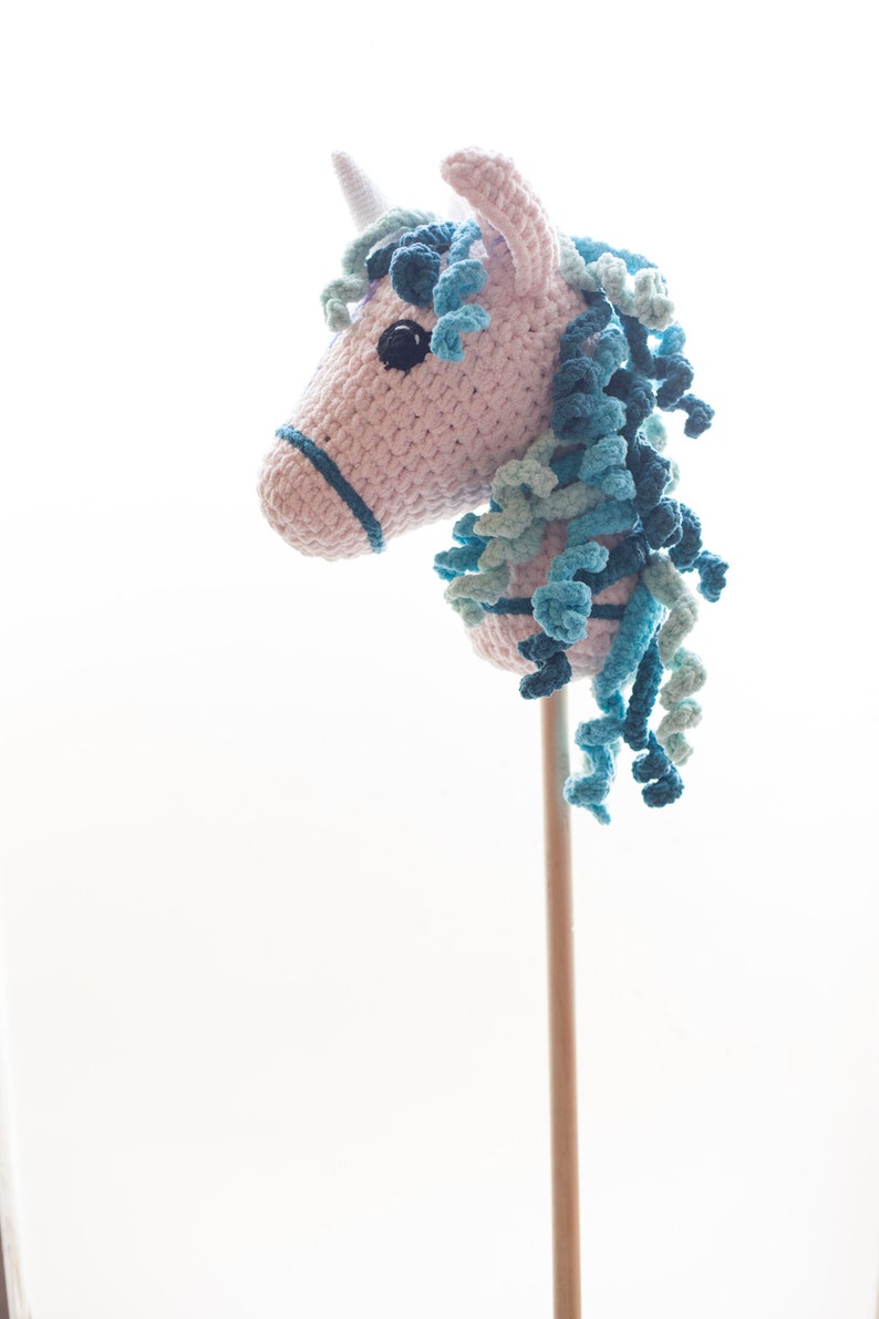 May include: A pink and blue crocheted unicorn hobby horse with a wooden stick.