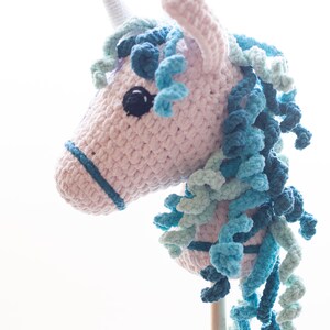 May include: A pink and blue crocheted unicorn head on a wooden stick. The unicorn has a blue and green mane and a white horn.