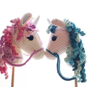 May include: Two crocheted unicorn rocking horses, one with pink and purple mane and the other with blue and green mane, facing each other.