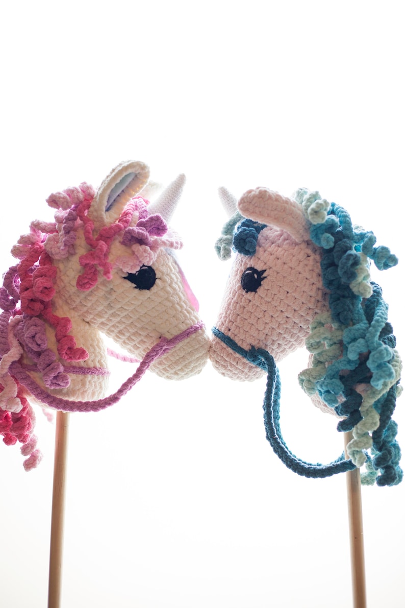 May include: Two crocheted unicorn rocking horses, one with pink and purple mane and the other with blue and green mane, facing each other.