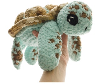 May include: A crocheted sea turtle plush toy with a brown and beige shell and a light blue body. The toy has black eyes and a friendly expression.