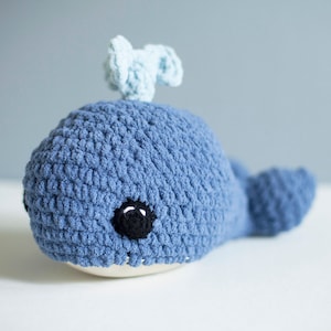 May include: A blue crocheted whale stuffed animal with black eyes and a light blue crocheted fin on top of its head.