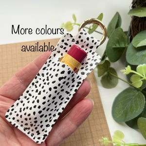 Può includere: Un portachiavi bianco con pois neri, con un anello portachiavi dorato e un balsamo per le labbra all'interno. Altri colori disponibili.