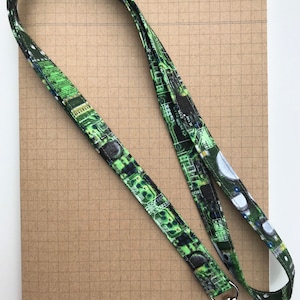 May include: A green and black lanyard with a circuit board pattern. The lanyard has a silver swivel clasp.