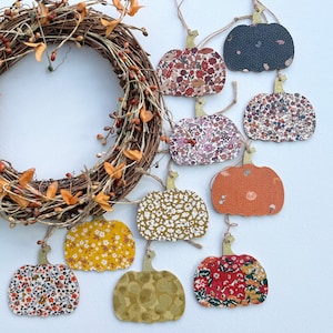 May include: Nine fabric pumpkin ornaments with various floral patterns in shades of red, orange, yellow, blue, and green. The ornaments are hanging from a twig wreath.