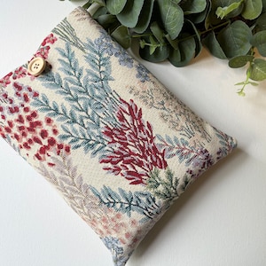 May include: A beige fabric pouch with a floral pattern in shades of red, blue, and green. The pouch has a single button closure.