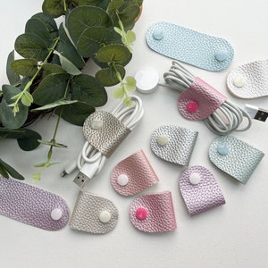 Peut inclure: Assortiment d'organisateurs de cordon en cuir de diff&eacute;rentes formes et tailles. Les organisateurs sont faits d'un mat&eacute;riau textur&eacute; et chatoyant et ont une fermeture &agrave; bouton.