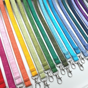 May include: A collection of fabric lanyards arranged in a spectrum of colours including red, pink, orange, yellow, light green, dark green, teal, light blue, medium blue, dark blue, purple, and grey, each featuring a silver metal swivel lobster clasp.