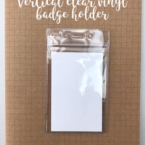 May include: A vertical clear vinyl badge holder on a brown gridded background. The holder has two eyelets at the top and a clear plastic flap that closes with a zipper.