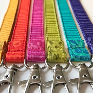 May include: Six colourful fabric keychains with striped patterns and floral designs. Each keychain has a silver swivel clasp.