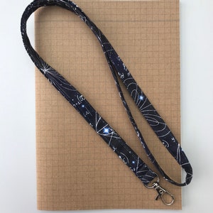 May include: A black lanyard with a white constellation pattern and mathematical equations. The lanyard has a silver swivel clip.
