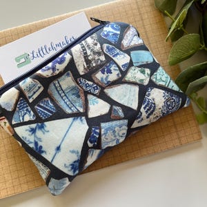 May include: A blue and white zippered pouch with a mosaic pattern of broken porcelain pieces. The pouch is made of fabric and has a zipper closure.