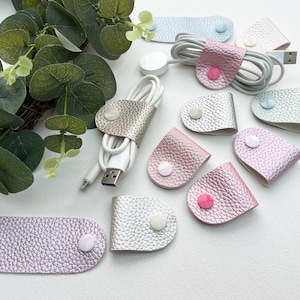 Peut inclure: Assortiment d'organisateurs de cordon en cuir de diff&eacute;rentes couleurs avec une fermeture &agrave; bouton blanc. Les organisateurs sont de formes et de tailles vari&eacute;es, notamment des formes ovales et en forme de larme.