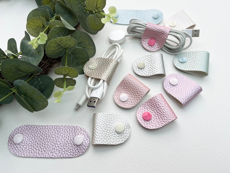 Peut inclure: Assortiment d'organisateurs de cordon en cuir de diff&eacute;rentes couleurs avec une fermeture &agrave; bouton blanc. Les organisateurs sont de formes et de tailles vari&eacute;es, notamment des formes ovales et en forme de larme.