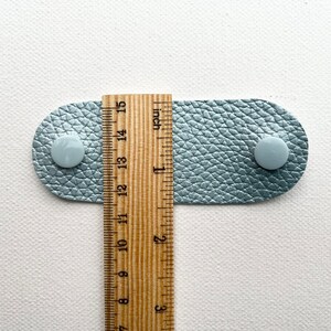 Peut inclure: Une sangle en cuir bleu clair avec deux boutons blancs et une r&egrave;gle en bois mesurant 3,8 cm.