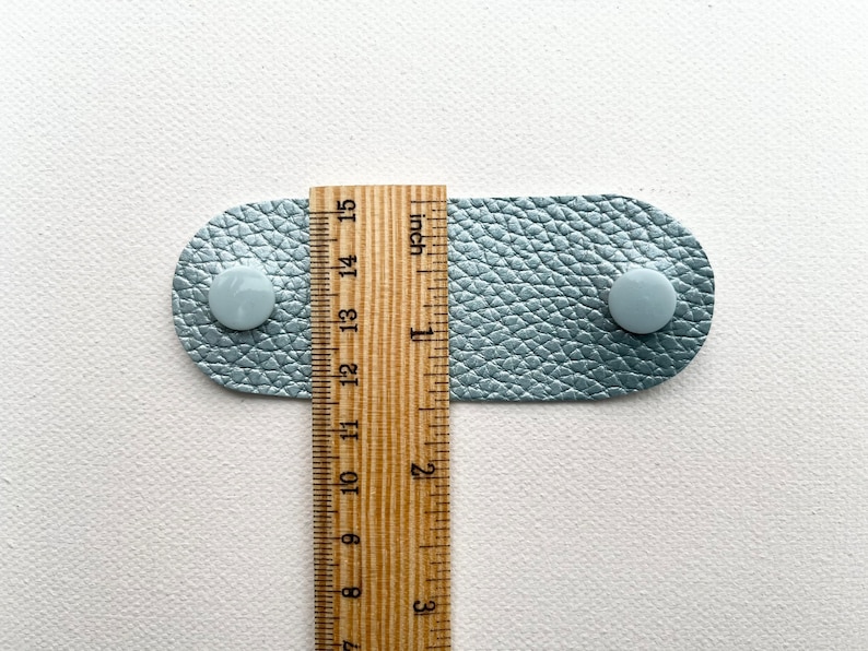 Peut inclure: Une sangle en cuir bleu clair avec deux boutons blancs et une r&egrave;gle en bois mesurant 3,8 cm.