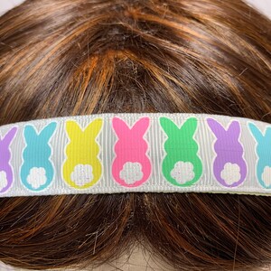 Puede incluir: Diadema blanca con un patr&oacute;n repetido de siluetas de conejos pastel. Los conejos son en tonos de rosa, verde, amarillo, azul y morado.