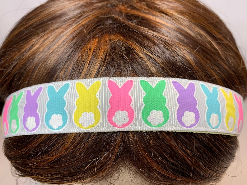 Puede incluir: Diadema blanca con un patr&oacute;n repetido de siluetas de conejos pastel. Los conejos son en tonos de rosa, verde, amarillo, azul y morado.