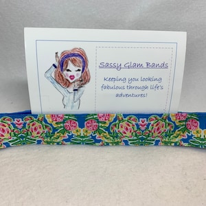 May include: A blue and white patterned hair tie with a card that says "Sassy Glam Bands! Keeping you looking fabulous through life's adventures!" and a cartoon illustration of a woman with brown hair wearing a blue headband.